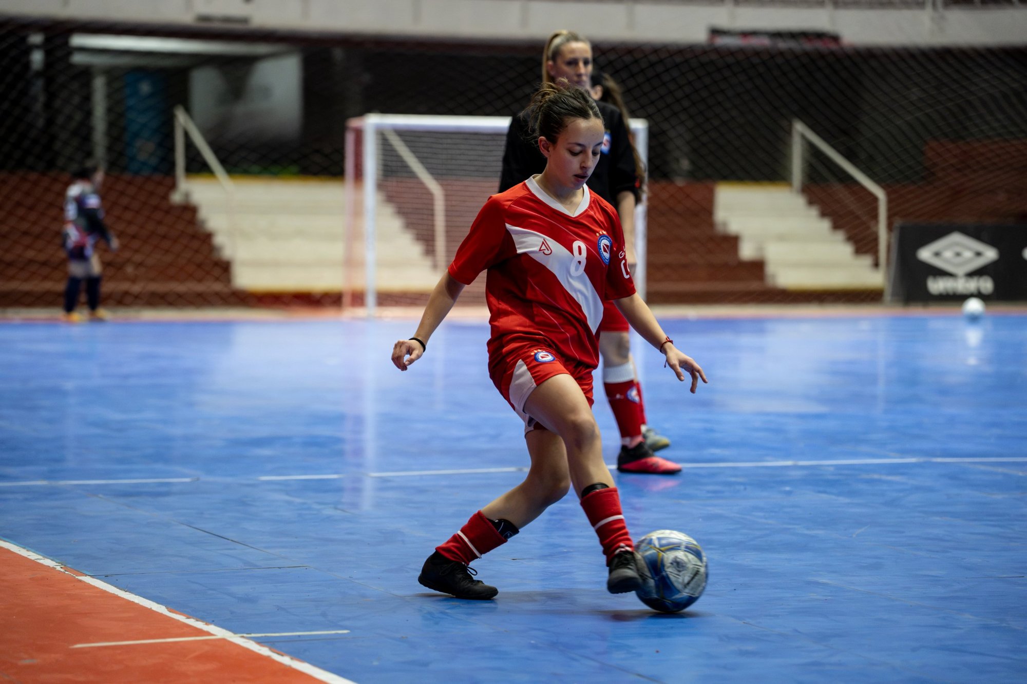 Home Jugadora de futsal con camiseta roja número 8 conduciendo la pelota sobre la cancha azul